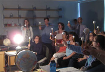 Teachers hold up a ball on a stick and visually observe the phases of the moon illuminated from a nearby lamp