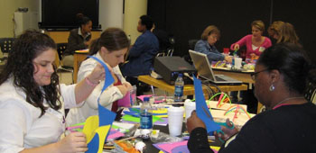 Teachers sit around tables and assemble by hand, workshop materials